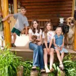 Kids and dogs on a porch with log cabin.