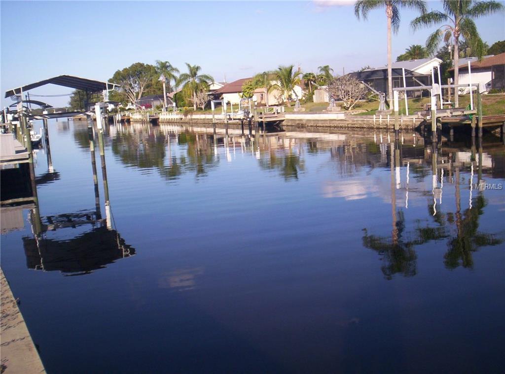 Calm water reflecting houses and palm trees.