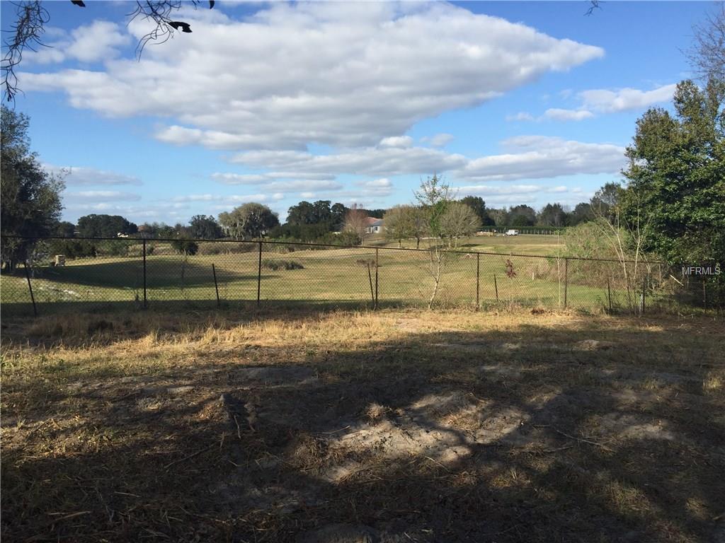 Fenced grassy field with trees and a house in the distance.