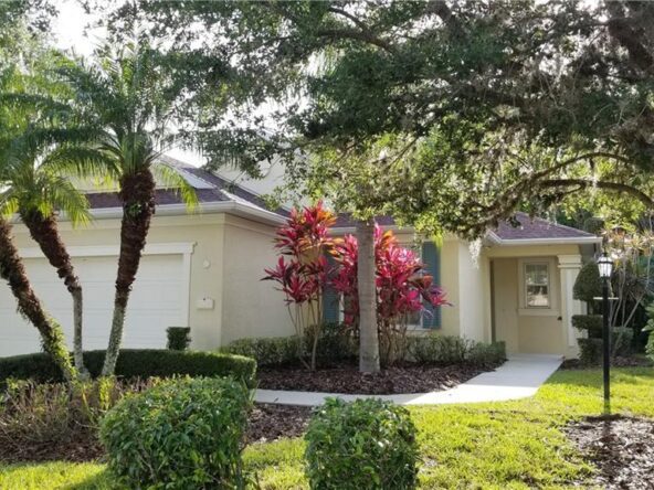 A tan house with palm trees and red plants.