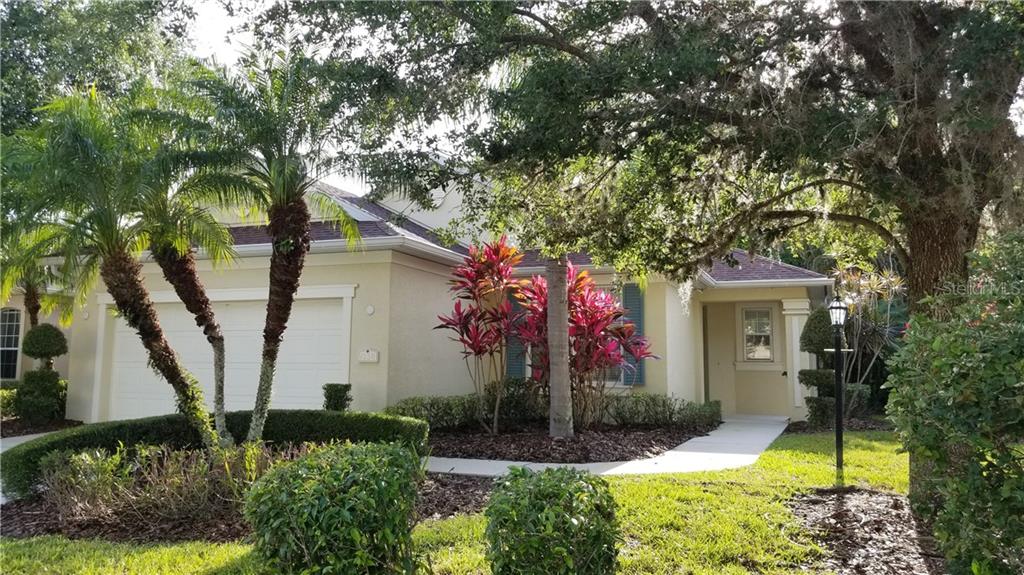 A beige house with palm trees and red foliage.