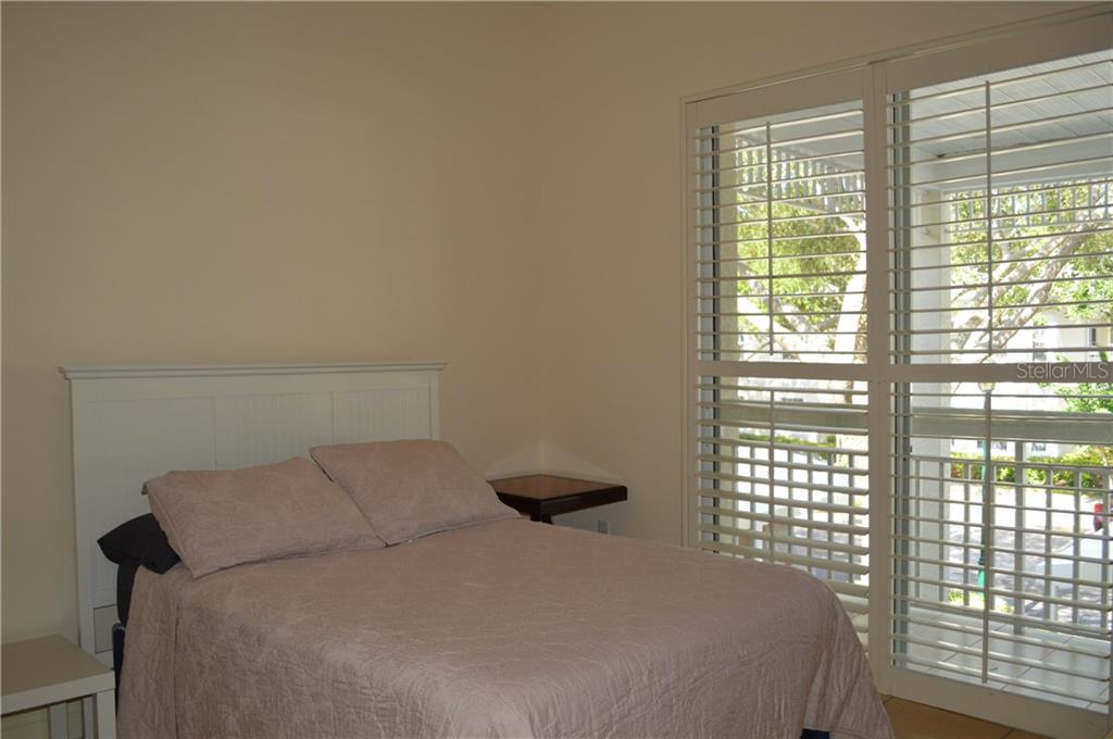 White bed with beige bedding and window shutters.