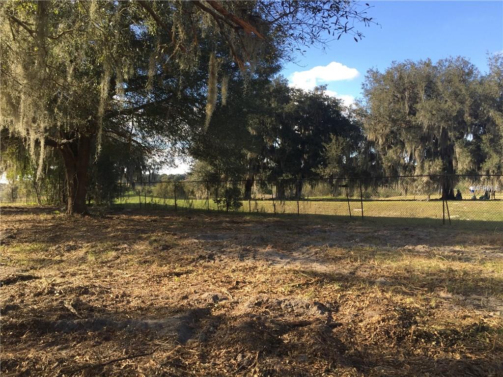 Open grassy field with trees and fence.