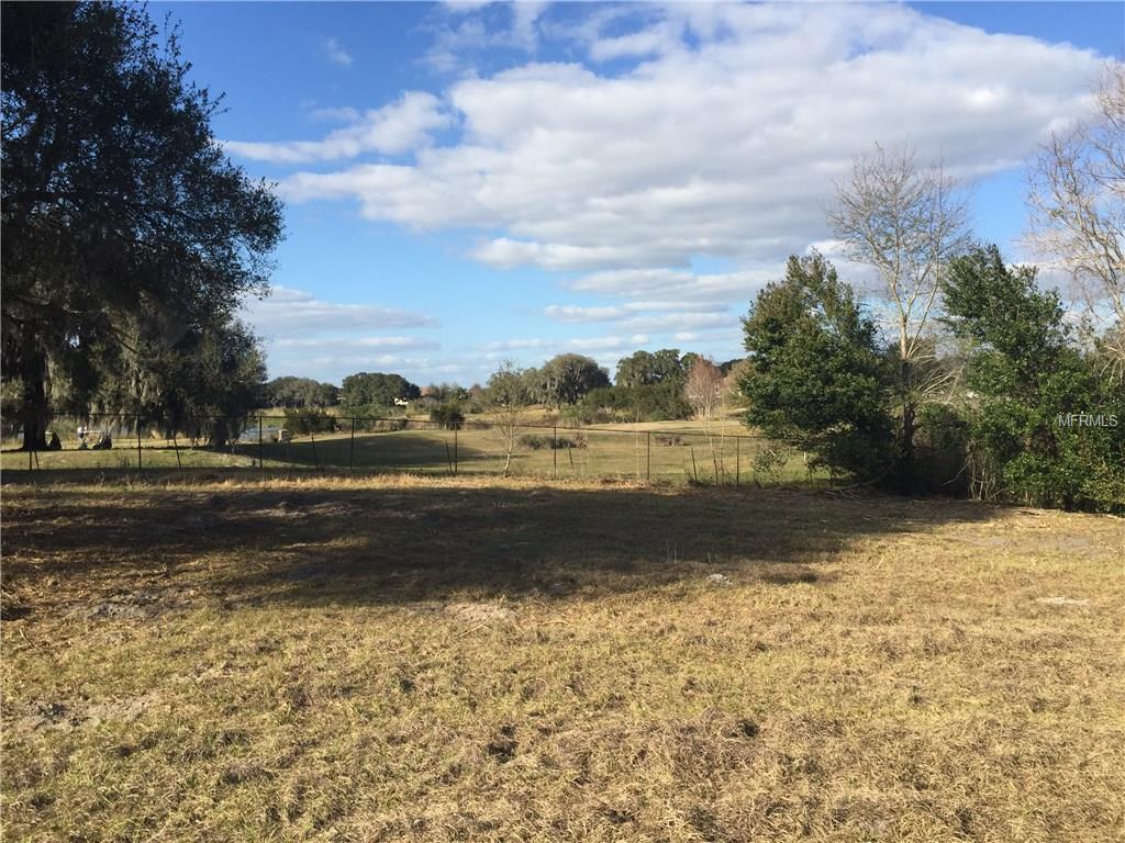 Open grassy field with trees and a fence.