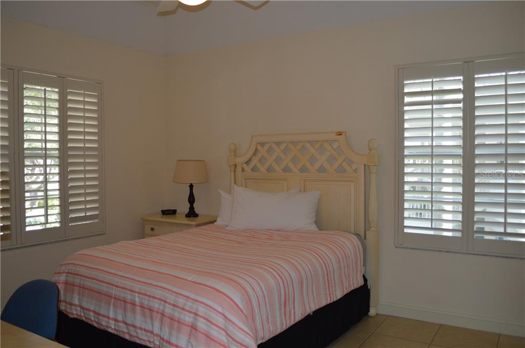 A bedroom with a striped bed and white shutters.