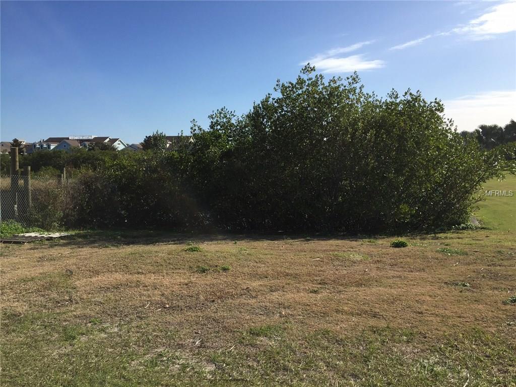 Empty grassy lot with bushes in background.