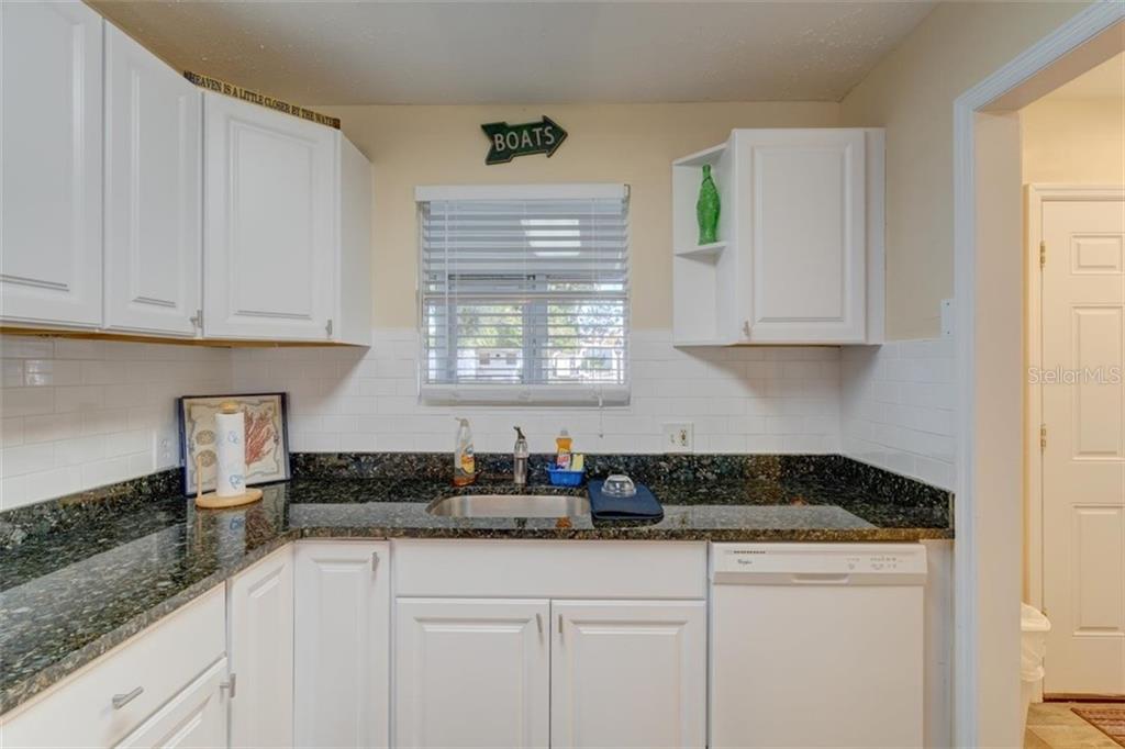 White kitchen with black countertops and a window.