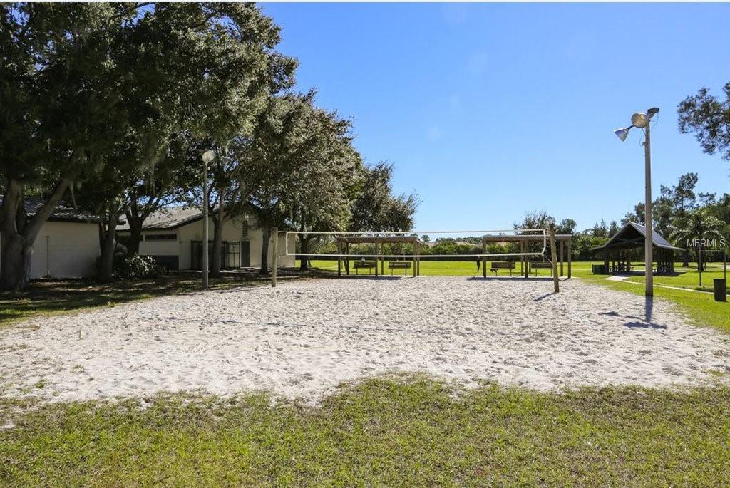 Sand volleyball court with trees and a building.