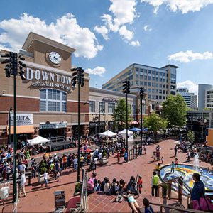 Crowded downtown square with fountain and shops.