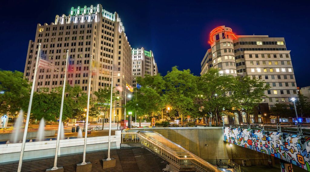 Cityscape with buildings and fountain at night.