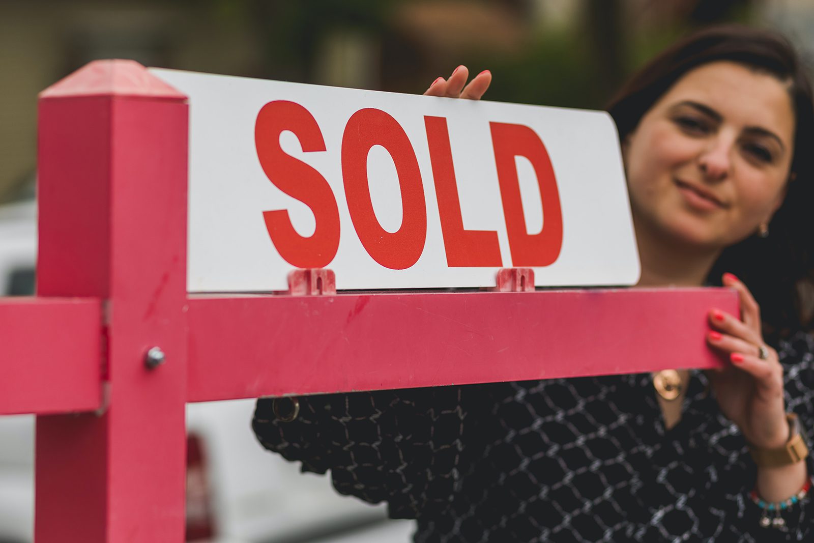 Woman holding a red sold sign.