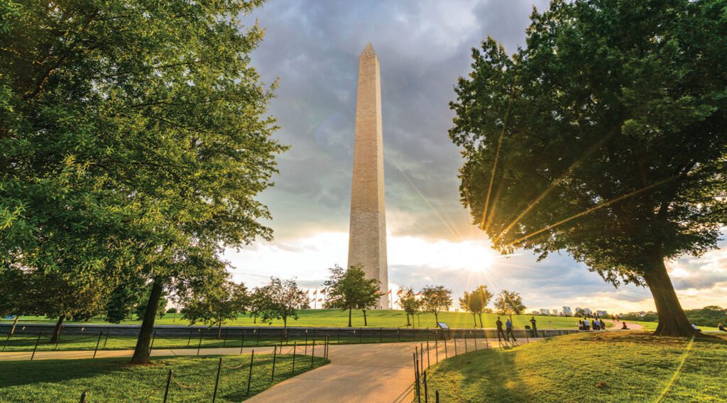 Washington Monument with trees and sun rays.