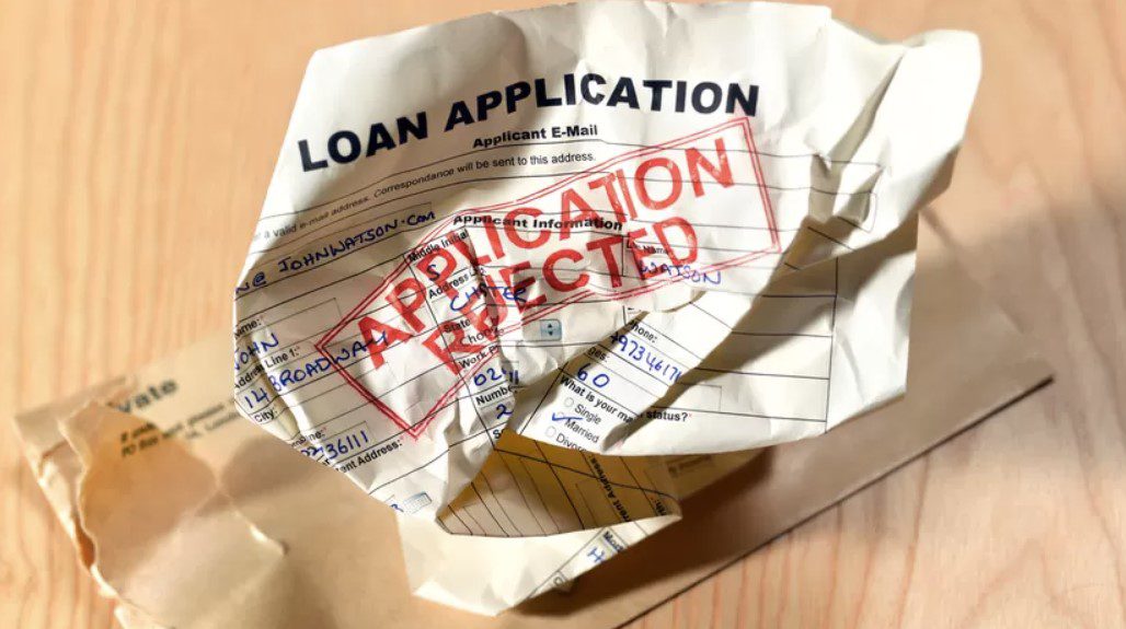 Rejected loan application crumpled on table.