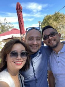 Three friends smiling under a red umbrella.