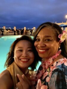 Two women smiling by a pool at night.